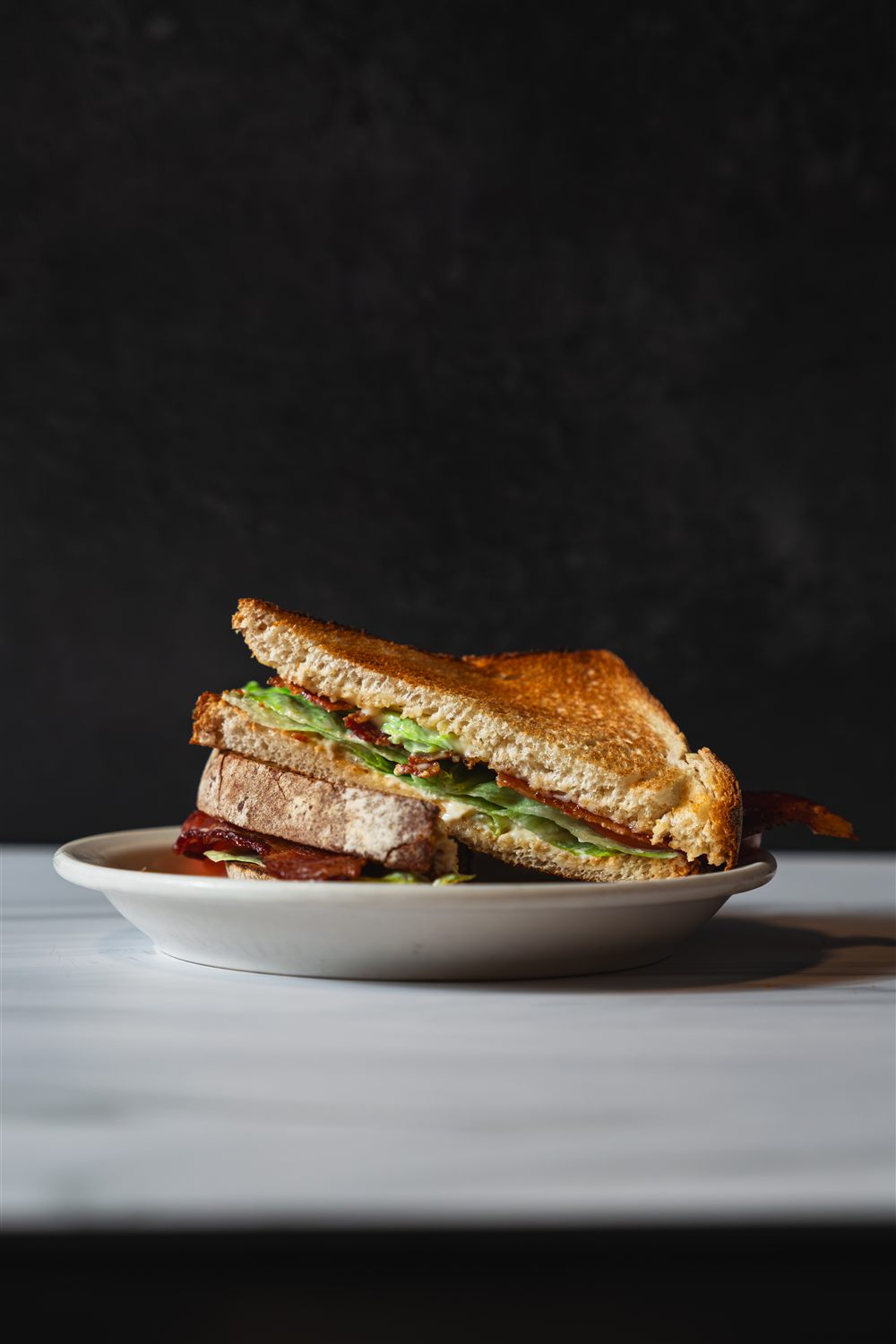 A BLT on toasted bread, bacon poking out the sides, stacked on a diner plate