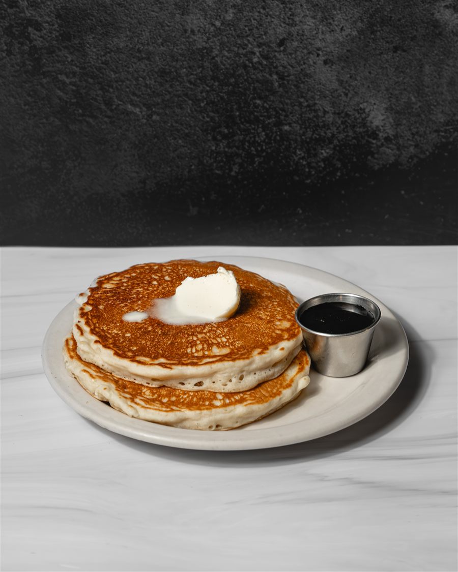Golden pancakes with a pat of butter and a cup of syrup