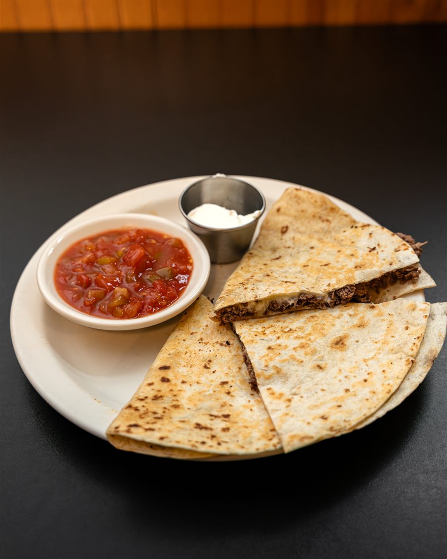 A breakfast quesadilla sliced in wedges with salsa and sour cream