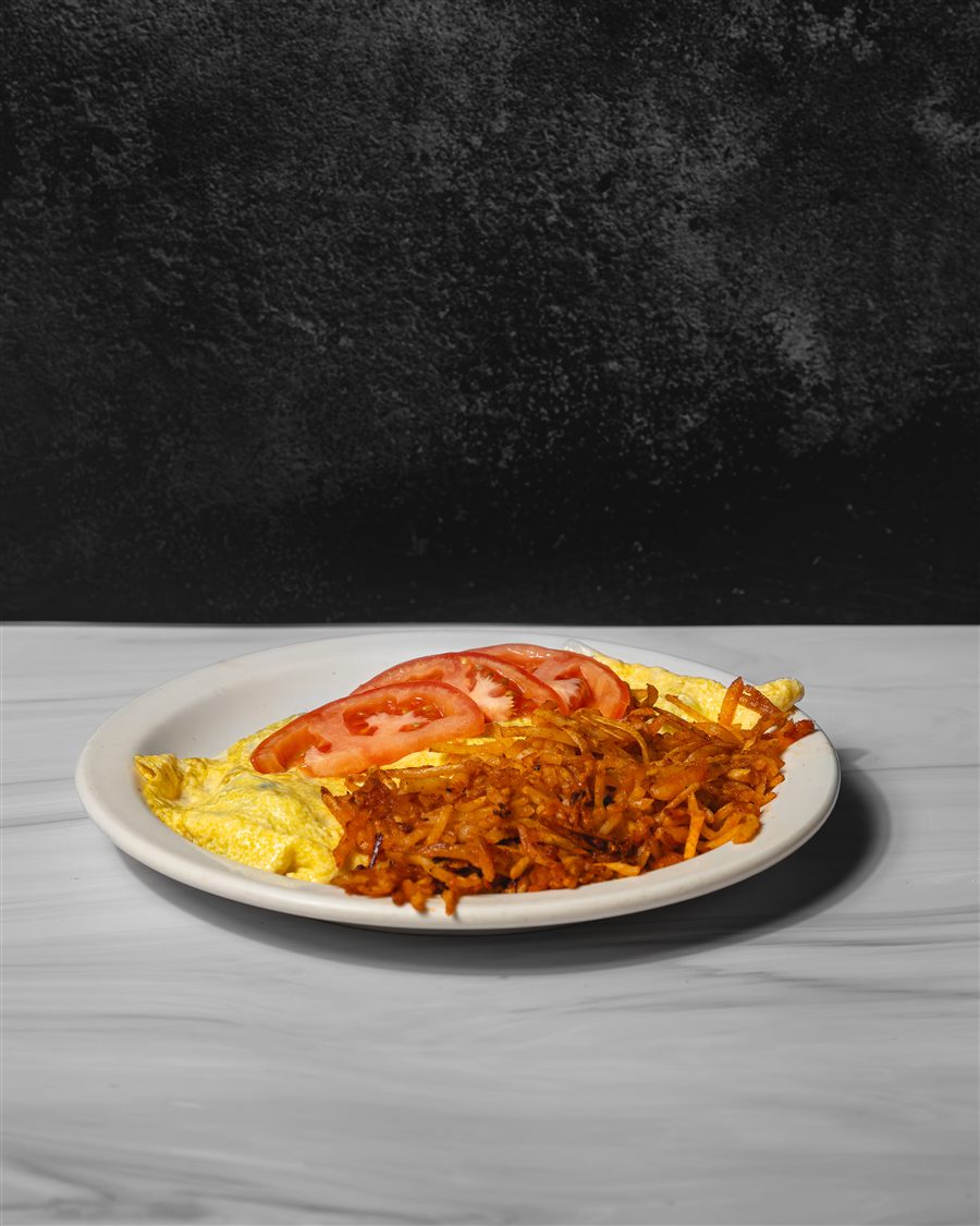 A folded omelette topped with tomato beside shredded hash browns