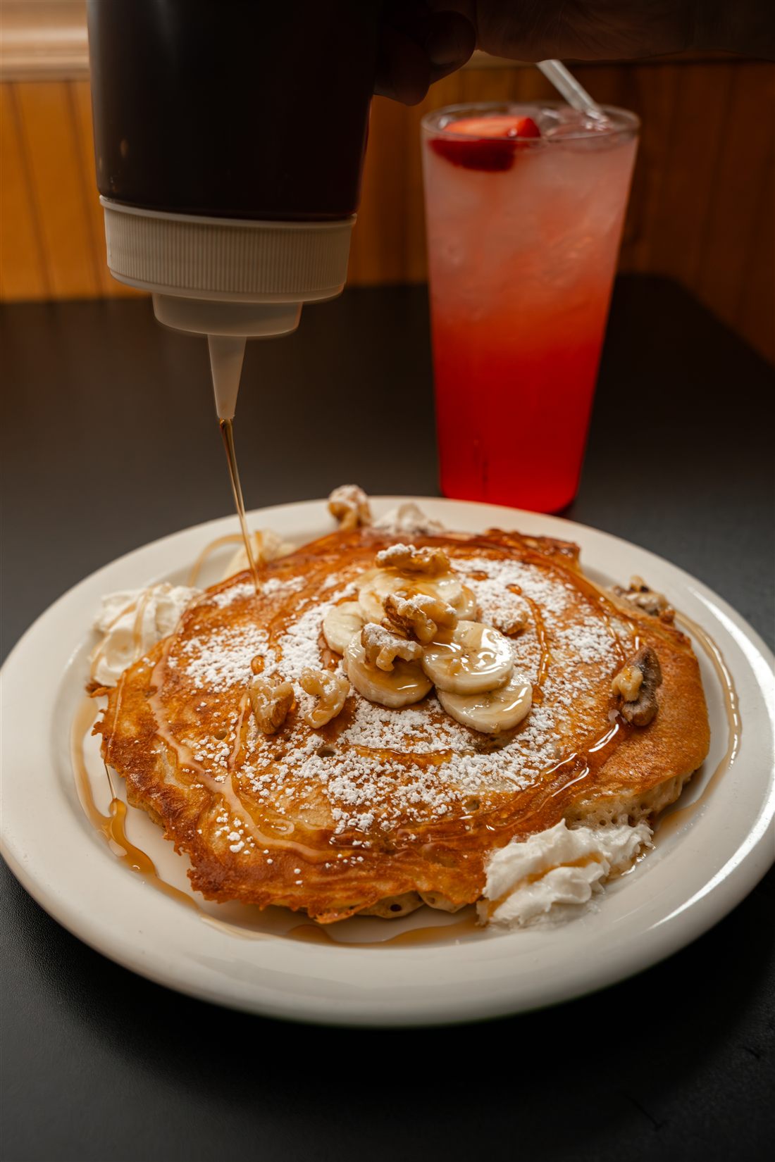 A banana walnut pancake with whipped cream, warm syrup being poured over the top